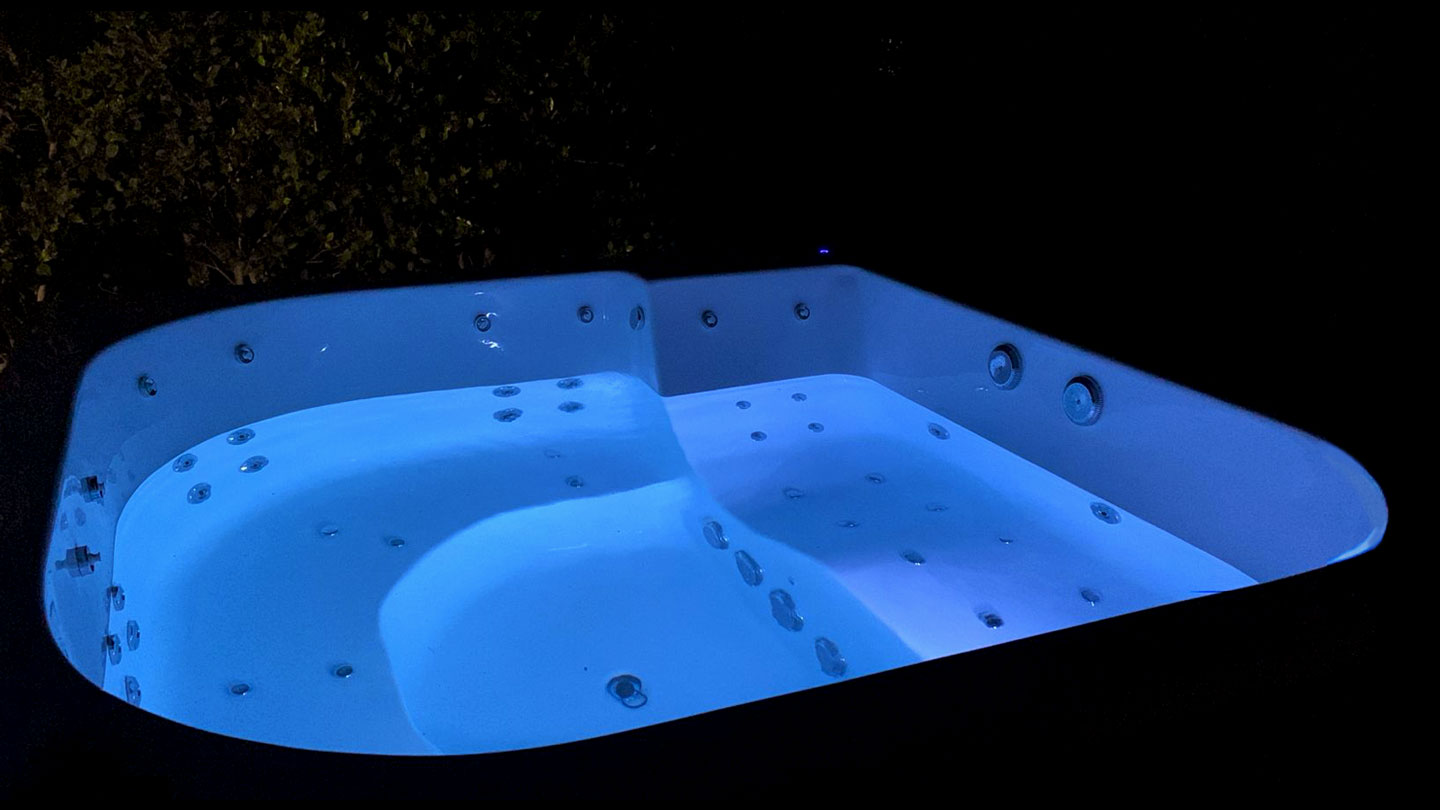 Amplia bañera de hidromasaje de diseño ergonómico con iluminación LED azul intensa, capturada en un entorno nocturno.