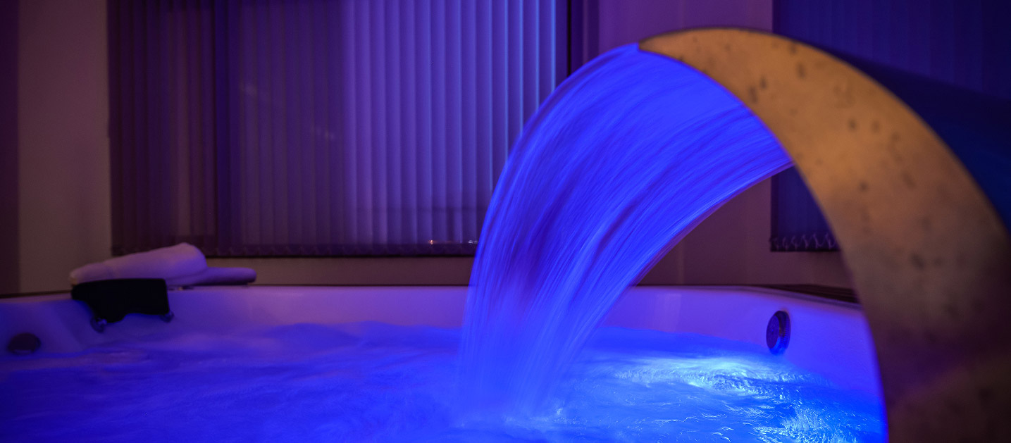 Primer plano de una cascada de acero fluyendo hacia una bañera de hidromasaje iluminada con una intensa luz led azul.